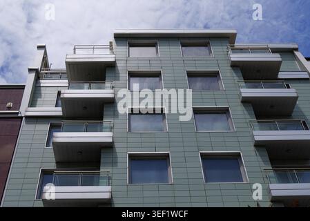 Die Außenfassade des modernen Wohngebäudes zeigt eine geometrische grüne Fassade mit zahlreichen Fenstern und Balkonen, die moderne Archi widerspiegeln Stockfoto