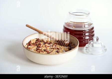 Frühstücksflocken mit Milch und Honig in einer Keramikschale auf weißem Hintergrund. Stockfoto