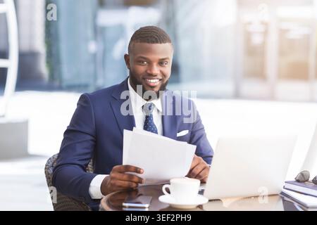Schwarzer Geschäftsmann arbeiten mit Papieren und Laptop im Café im Freien Stockfoto