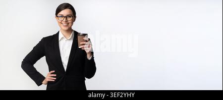 Selbstbewusste Geschäftsfrau, die Kaffee hält, während sie vor einem schlichten Hintergrund steht Stockfoto