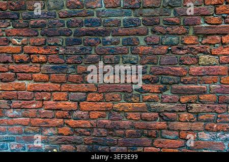 Eine direkte Nahansicht einer authentischen alten Ziegelmauer mit einer reichen, mehrfarbigen Textur aus roten, orangen und dunklen verwitterten Ziegeln. Die roug Stockfoto