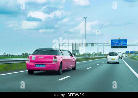 Niederlande - 17. April 2026: Eine markante, pinkfarbene Stretchlimousine fährt tagsüber über über eine niederländische Autobahn, die vor einem Hintergrund in Bewegung gehalten wird Stockfoto
