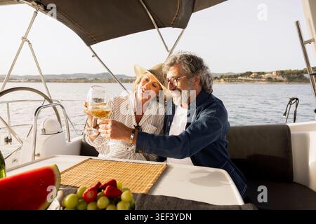 Glückliches, reifes Paar auf einer Jacht, das während der Sommerferien mit Weißwein toast Stockfoto