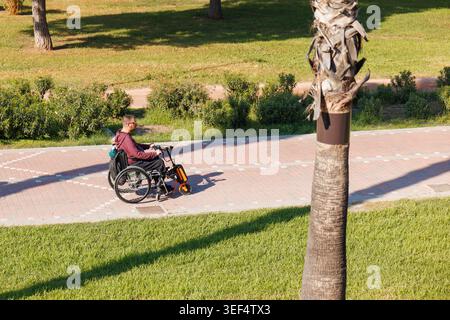 Mann im Rollstuhl, der auf einem zugänglichen Fahrradweg mit Mobilitätsbefestigung fährt, wobei er die unabhängige Mobilität, Zugänglichkeit und Inklusivität der Stadt hervorhebt Stockfoto