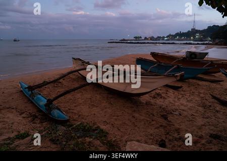 Traditionelle Sri-lankische Auslegerboote ruhen in der Abenddämmerung an einem Sandstrand unter dem bewölkten, dämmerlichen Himmel in Tangalle, Sri Lanka Stockfoto