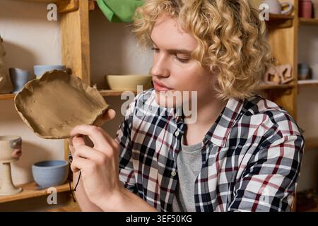 Ein erfahrener junger Töpfer formt sorgfältig Ton in einer pulsierenden Töpferwerkstatt voller Kunst. Stockfoto