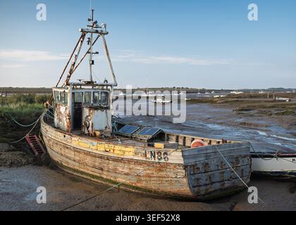 Ein altes hölzernes Fischerboot stützte sich während der Ebbe in Brancaster, Norfolk, England auf den trockenen Wattbänken Stockfoto