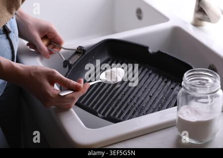 Frau, die Backpulver benutzt, um Pfanne drinnen zu grillen, Nahaufnahme Stockfoto