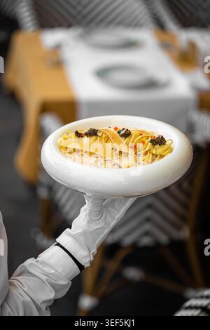 Der Kellner serviert Gourmet-Pasta in einer weißen Schüssel Stockfoto