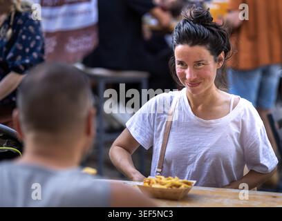 Dijon, Frankreich - 9. Mai 2026: Eine lächelnde junge Frau sitzt mit einem Mann an einem Restauranttisch im Freien. Ein Paar, das Pommes frites teilt und ein Konversation hat Stockfoto