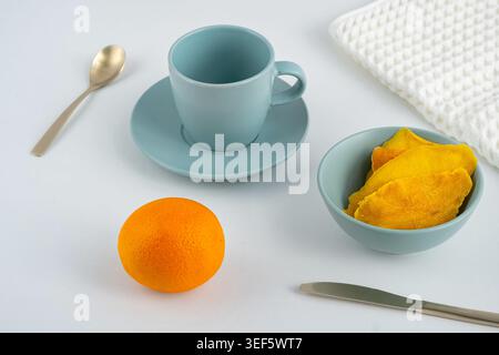 Helles orangenes Obst und blaues Geschirr auf einem einfachen Tisch in einem Küchenbereich Stockfoto