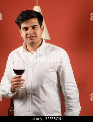Mann hält Rotweinglas mit Blick auf die Kamera, selbstbewusstes Lifestyle und Gastfreundschaft Konzept in Studio-Umgebung Stockfoto