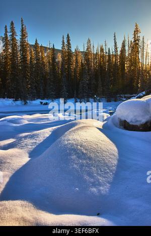 Schneebedeckter Sonnenaufgangswald und gefrorener Fluss in der Winterlandschaft Stockfoto