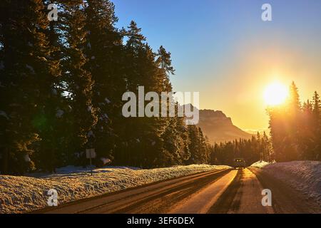 Winter Road Sonnenaufgang im verschneiten Kiefernwald mit Blick auf die Berge Stockfoto