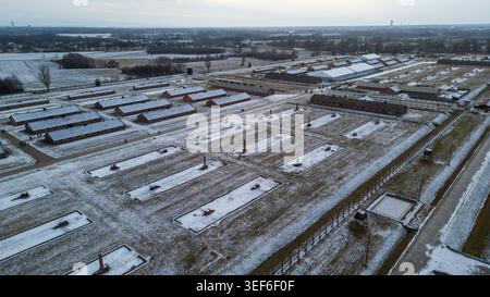 Ein Hochwinkel-Drohnenschuss zeigt historische Kasernen und verbliebene Ziegelschornsteine im Vernichtungslager Birkenau. Der Boden ist teilweise bedeckt Stockfoto