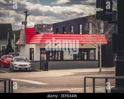 Kleines Fast-Food-Restaurant mit markantem rotem Dach und Fenstern in der Stadt mit Autos und bewölktem Himmel Stockfoto