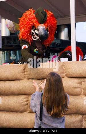 Waggis auf einem Karnevalswagen, der einem Kind Geschenke an der Basler Fasnacht 2026 in Basel, Schweiz, überreicht Stockfoto