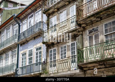 Nahaufnahme historischer Hausfassaden in Porto, Portugal, mit kunstvoll verzierten schmiedeeisernen Balkonen, traditionellen blauen Azulejo-Fliesen und Steinmauern Stockfoto