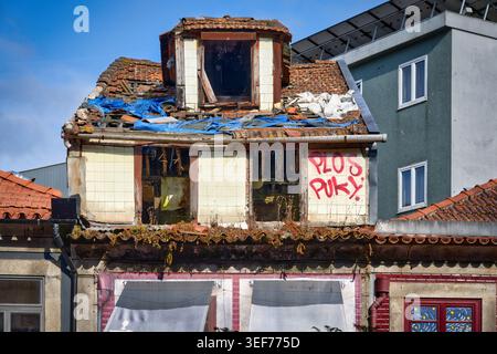 Porto, Portugal 13. Juni 2025: Das obere Stockwerk eines alten Hauses in Porto mit einem eingestürzten Dach, einer blauen Plane, Graffiti und kaputten Fenstern wurde schwer beschädigt Stockfoto