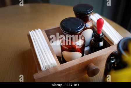 Rustikaler hölzerner Conditioner Caddy, der auf einem hölzernen Kaffeetisch sitzt. Auf dem Tablett befinden sich gefaltete weiße Papierservietten und ein dunkler Glasapothekenboden im Vintage-Stil Stockfoto