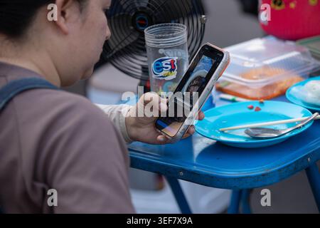 PHAYAO, THAILAND-APR 11, 2026: Frau, die ihr Smartphone im Ruhezustand benutzt, tägliche Smartphone-Aktivität, moderne städtische Routine, Nahaufnahme, Chiang Kham. Stockfoto
