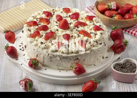 Kuchen mit Erdbeeren, Sahne und Schokolade auf einem Holztisch umgeben von frischen Erdbeeren Stockfoto