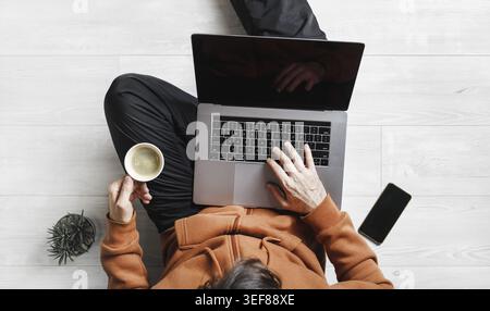 Geschäftsmann arbeitet zu Hause während der Coronavirus-Pandemie. Freelancer mit Laptop arbeitet, während er auf dem Boden sitzt. Online-Schulung Stockfoto