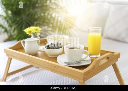 Holztablett mit Frühstück auf dem Bett in einem Hotelzimmer, romantischer Morgen mit gesundem Essen Stockfoto