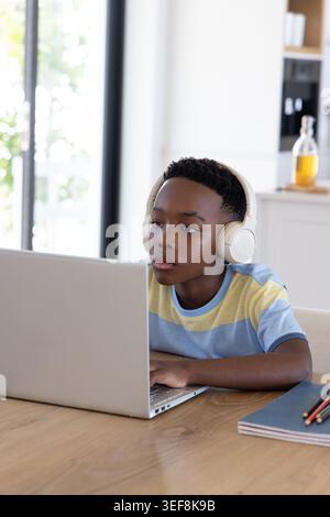 Afroamerikanischer Junge mit gestreiftem Hemd am Tisch in der Küche mit Laptop und Kopfhörern Stockfoto