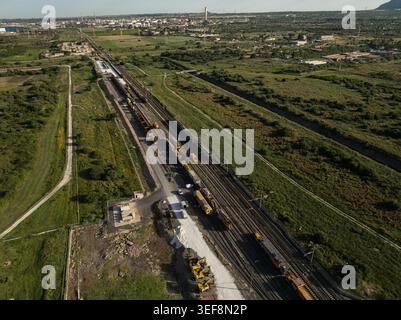 Aus der Vogelperspektive der Bahnwartungszüge auf Gleisen, die von grünen Feldern und industrieller Infrastruktur umgeben sind, in Priolo Gargallo, Sizilien, Italien. Stockfoto