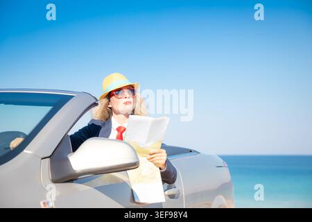 Erfolgreiche junge Geschäftsfrau am Strand. Frau, die im Oldtimer sitzt. Sommerurlaub und Freiheitsreisekonzept Stockfoto