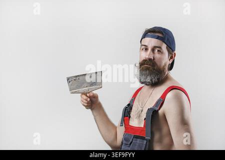 Builder mit Spachtel. Porträt eines bärtigen Mannes im Overall und einer Baseballmütze Stockfoto