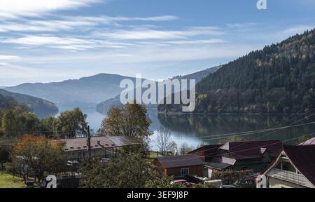 Ein ruhiger Blick auf den See Izvorul Muntelui, der an einem sonnigen Herbsttag in der Region Neamt in Rumänien die mit Kiefern bedeckten Karpaten reflektiert Stockfoto