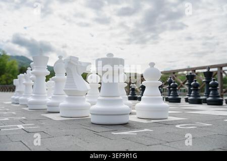 Riesige Plastikschachteile auf einem großen Freischachbrett in einem öffentlichen Park unter bewölktem Himmel, Geschäftsstrategiekonzept. Stockfoto