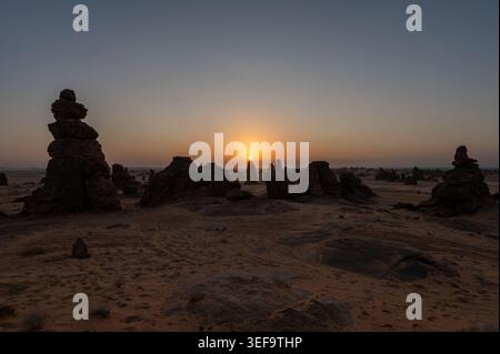 Steinklima und Sandsteinkulisse umgeben leuchtende Sonne am Horizont beim Sonnenuntergang in der Wüste, Alula Region, Saudi Arabien Stockfoto