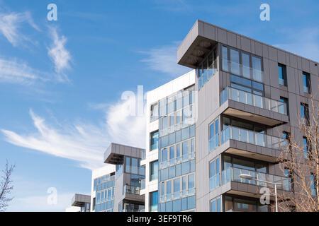 Eine nach oben gerichtete Aufnahme eines modernen mehrstöckigen Apartmentgebäudes mit einer eleganten grau-weißen Fassade, Glasbalkonen und großen Fenstern. Die Gegenwart Stockfoto