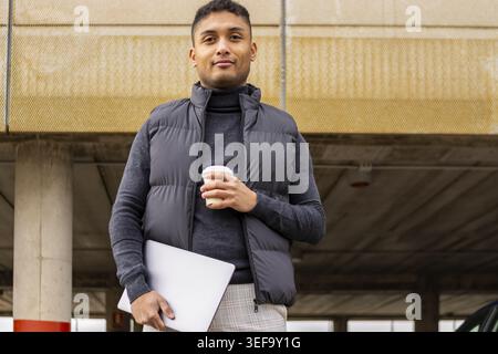 Porträt eines lächelnden lateinuniversitätslehrers mit Laptop und Kaffee in einer Pause im Freien Stockfoto