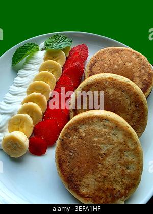 Pfannkuchen mit Banane, Erdbeere und Creme isoliert auf grünem Hintergrund Stockfoto