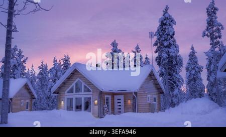 Schneebedeckte Holzhütten im finnischen Lappland bei farbenfrohen arktischen Wintersonnenvergnügen Stockfoto