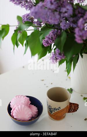 Minimales Stillleben mit süßen Marshmallows, Kaffeetasse und frischen Fliederblüten schaffen eine ruhige Frühlingsatmosphäre. Stockfoto