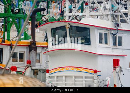 Yilan, Taiwan - 31. März 2025: Fischboot-Radhaus am Hafen von Nanfangao mit rot getrimmtem Rumpf, Blumenschmuck und Tintenfisch-Angellichtern über dem Hafen Stockfoto
