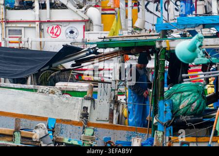 Yilan, Taiwan - 31. März 2025: Wanderfischer pflegen Netze zwischen vertäuten Schiffen in Nanfangao, was die Arbeitskräfte in Taiwans Fischereiindustrie hervorhebt. Stockfoto
