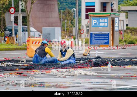 Yilan, Taiwan - 31. März 2025: Wanderfischer reparieren ein Fischernetz auf dem Gehweg in Nanfangao, das ausländische Arbeitskräfte in der taiwanischen Fischerei widerspiegelt. Stockfoto