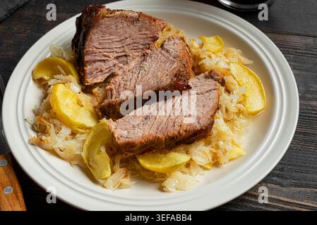 Gebratenes deutsches Schweinefleisch mit Äpfeln und Sauerkraut auf Teller, detaillierte Nahaufnahme. Schweinelendfleisch langsam kochen mit Apfel, Kohl. Bayerisches Oktoberfest Stockfoto