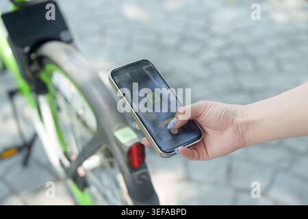 Asiatische Frau scannt QR-Code auf dem Smartphone, um gemeinsam genutztes Fahrrad im Freien zu mieten, Technologie Stockfoto
