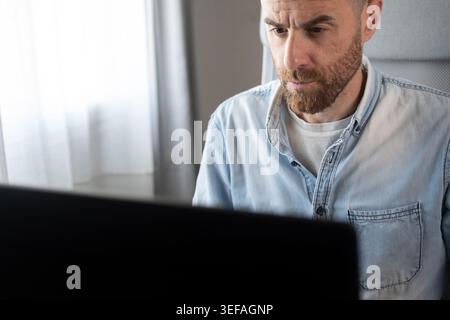 Konzentrierter Mann, der Desktop-Computer verwendet, während er von zu Hause aus arbeitet. Modernes Konzept für Business, Produktivität und Remote-Arbeit. Stockfoto