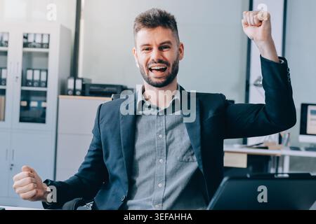 Der lächelnde Geschäftsmann im Anzug arbeitet in einem hellen, modernen Büro mit seinem Laptop Stockfoto