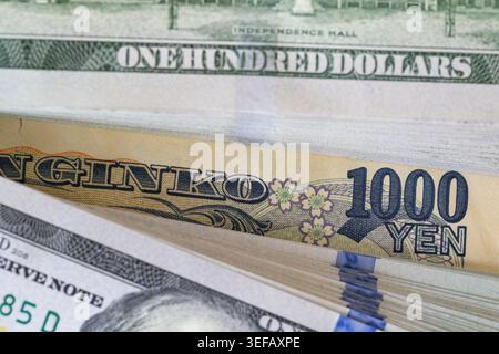 Ein japanischer 1000-Yen-Schein, der in einen Stapel mit 100-Dollar-Banknoten gesteckt wurde Stockfoto