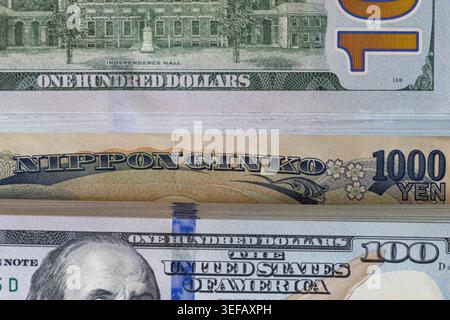 Ein japanischer 1000-Yen-Schein, der in einen Stapel mit 100-Dollar-Banknoten gesteckt wurde Stockfoto