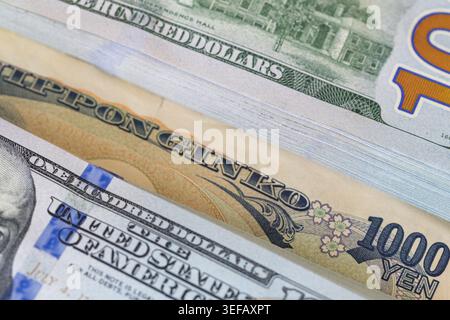 Ein japanischer 1000-Yen-Schein, der in einen Stapel mit 100-Dollar-Banknoten gesteckt wurde Stockfoto